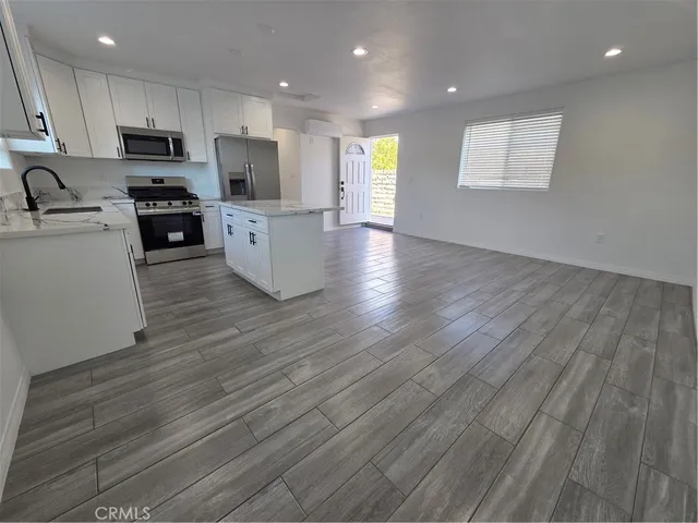 a kitchen with kitchen island granite countertop wooden floors white cabinets and stainless steel appliances