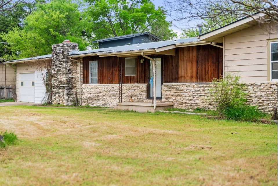 1100 Neans Drive Austin, TX 78758 - Photo 2 of 40 View of side of home with stone siding, board and batten siding, a garage, a yard, and a chimney