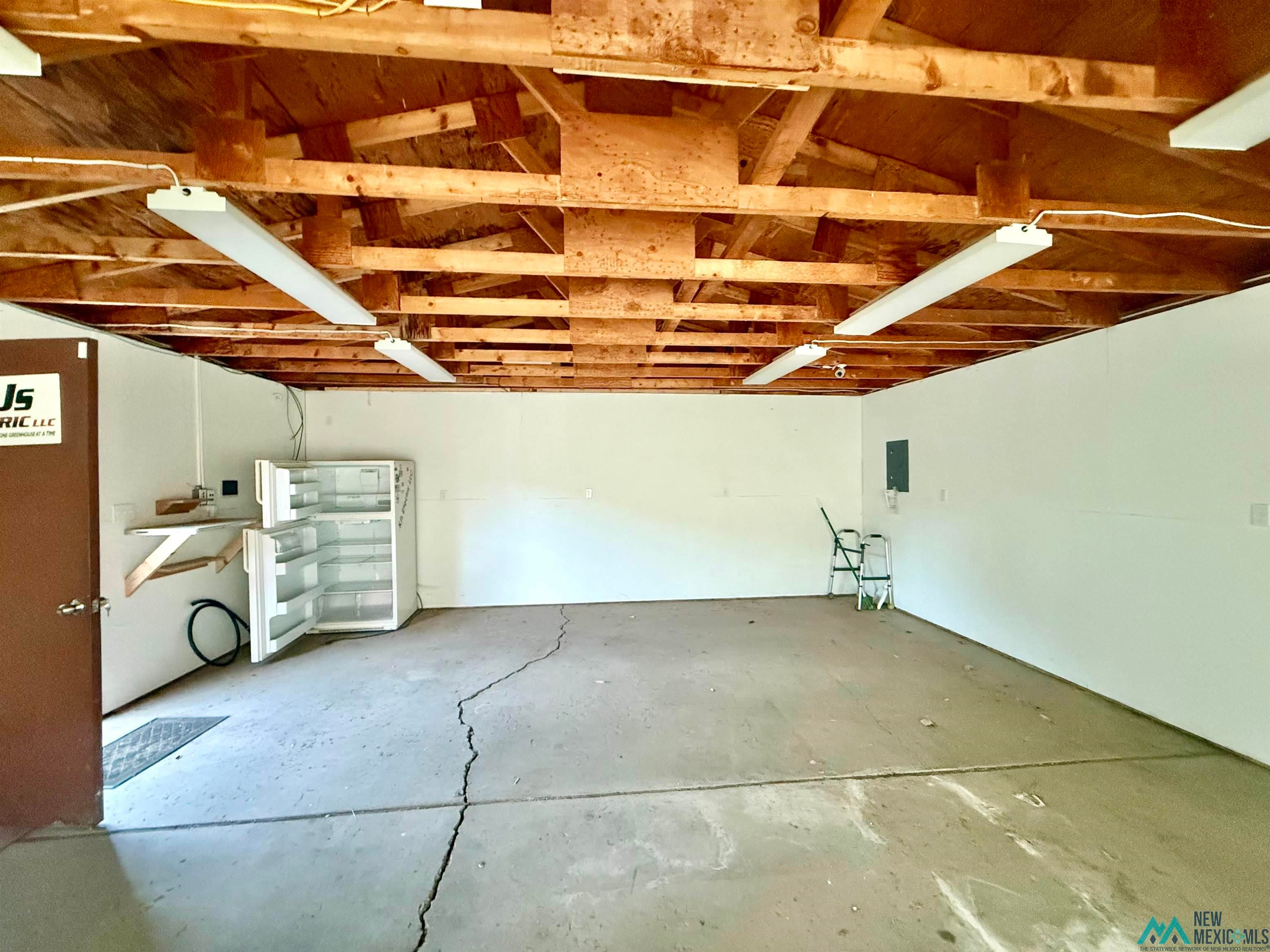 25 Linwood Road Raton, NM 87740 - Photo 5 of 41 Spacious interior with exposed ceiling joists, multiple fluorescent light fixtures, a white painted wall finish, and a concrete floor