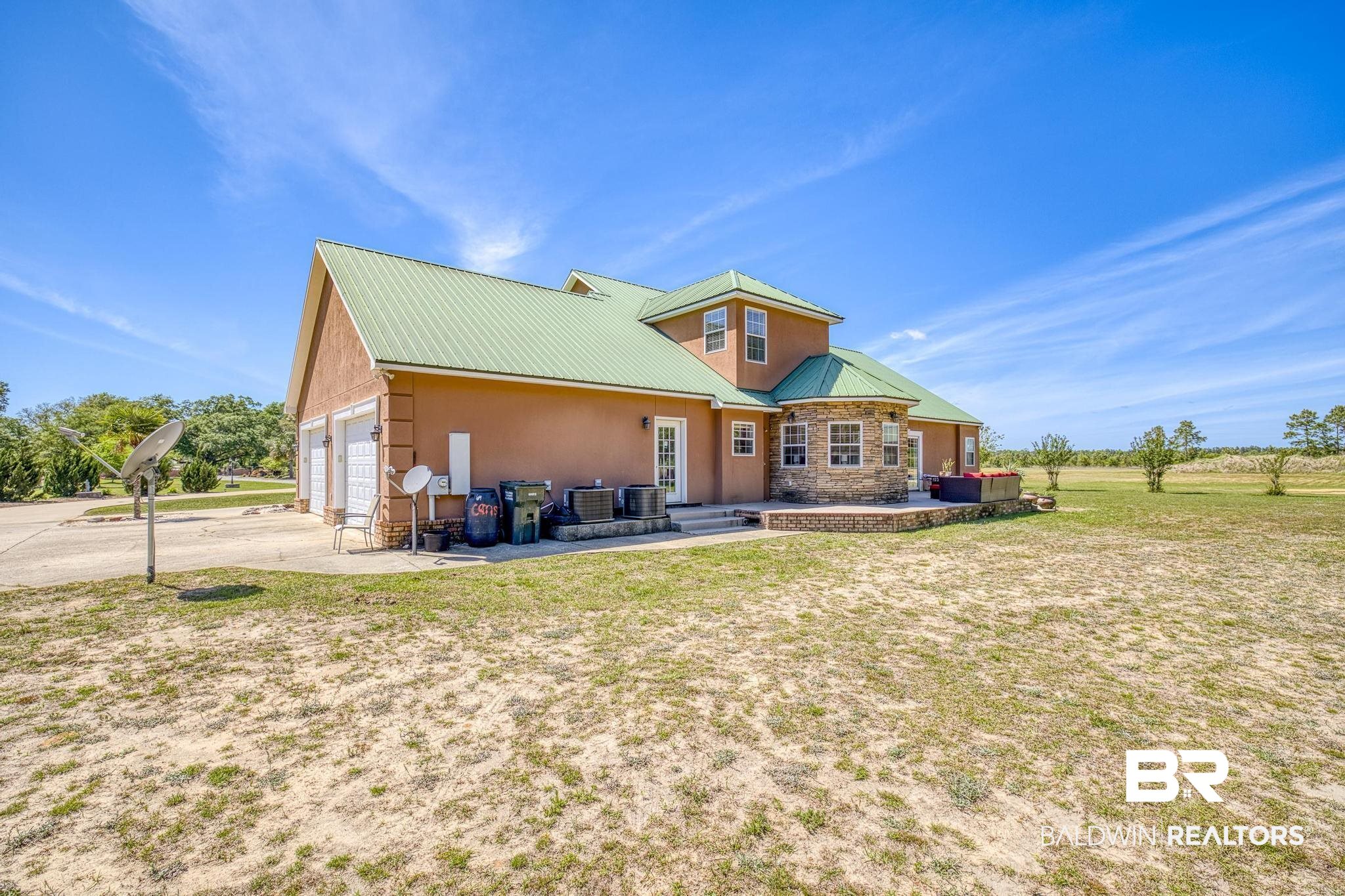 32875 Faircloth Road Lillian, AL 36549 - Photo 55 of 85 View of front facade featuring a metal roof, a patio area, a front lawn, stone siding, and driveway