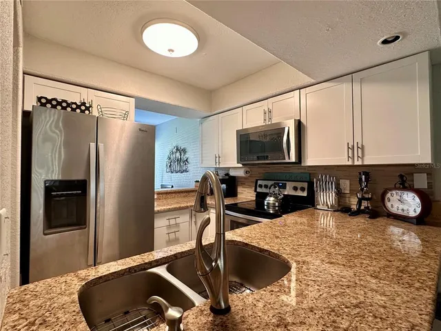 a kitchen with stainless steel appliances granite countertop a sink a refrigerator and a stove top oven