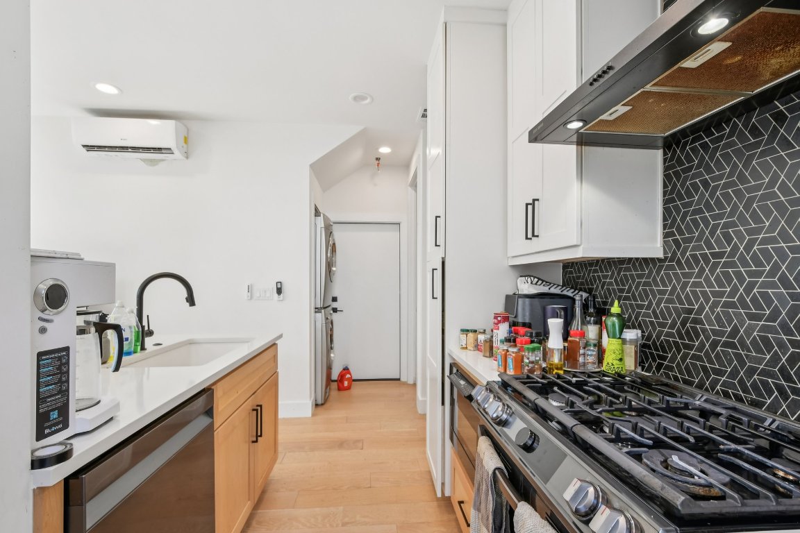 2916 East 13th Street, Unit 2 Austin, TX 78702 - Photo 10 of 35 Kitchen with appliances with stainless steel finishes, ventilation hood, decorative backsplash, light stone countertops, and light wood-style flooring