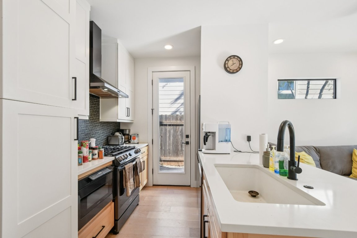 2916 East 13th Street, Unit 2 Austin, TX 78702 - Photo 8 of 35 Kitchen with white cabinets, wall chimney exhaust hood, black appliances, light wood-style floors, and decorative backsplash