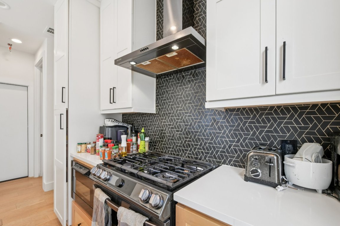 2916 East 13th Street, Unit 2 Austin, TX 78702 - Photo 9 of 35 Kitchen with wall chimney exhaust hood, stainless steel gas range oven, white cabinetry, and decorative backsplash