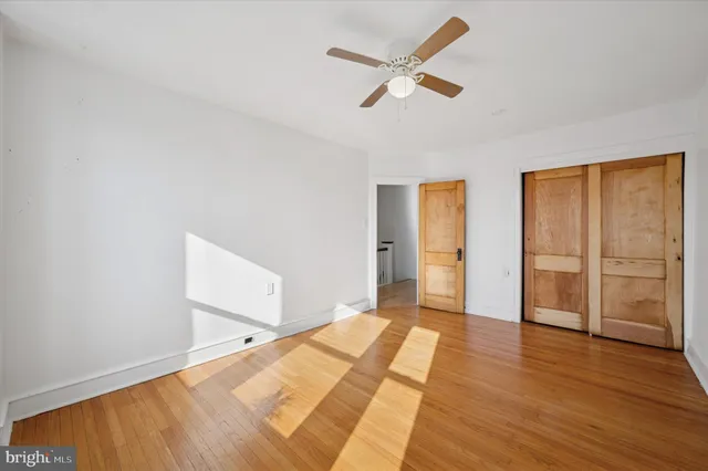 an empty room with wooden floor a ceiling fan and windows