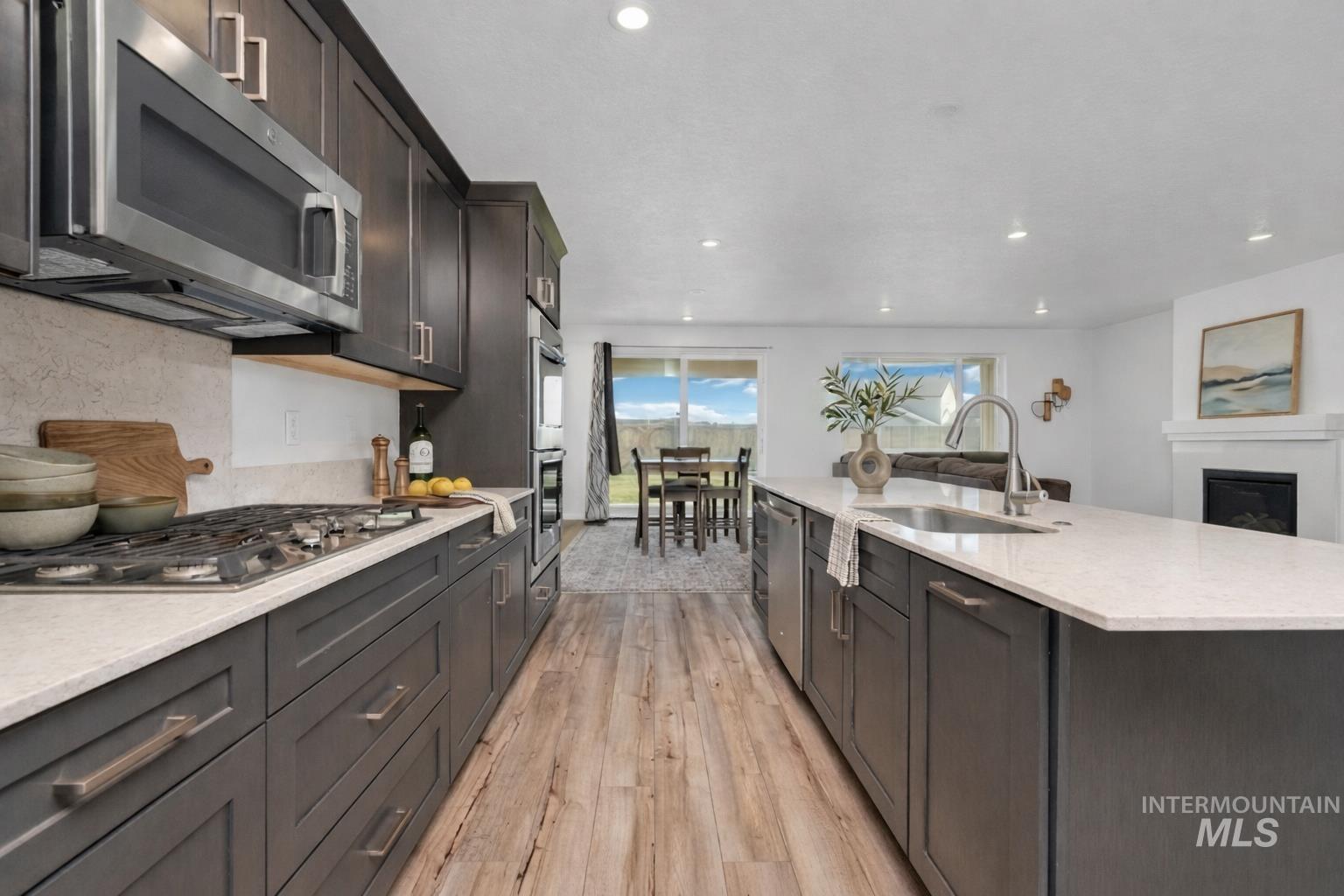 20430 Pitkin Way Caldwell, ID 83605 - Photo 6 of 23 Kitchen with light stone countertops, stainless steel appliances, light wood finished floors, a glass covered fireplace, and recessed lighting