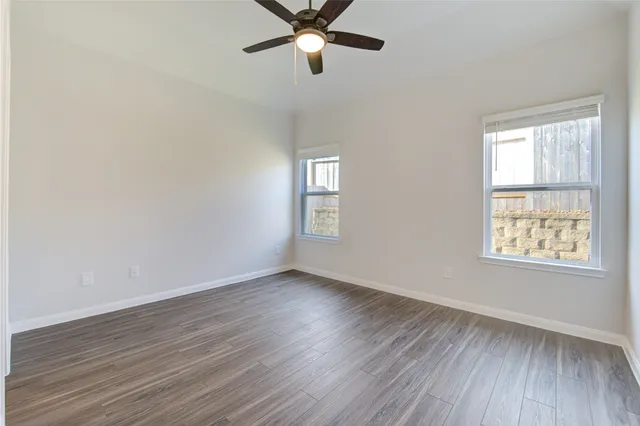 an empty room with wooden floor ceiling fan and windows