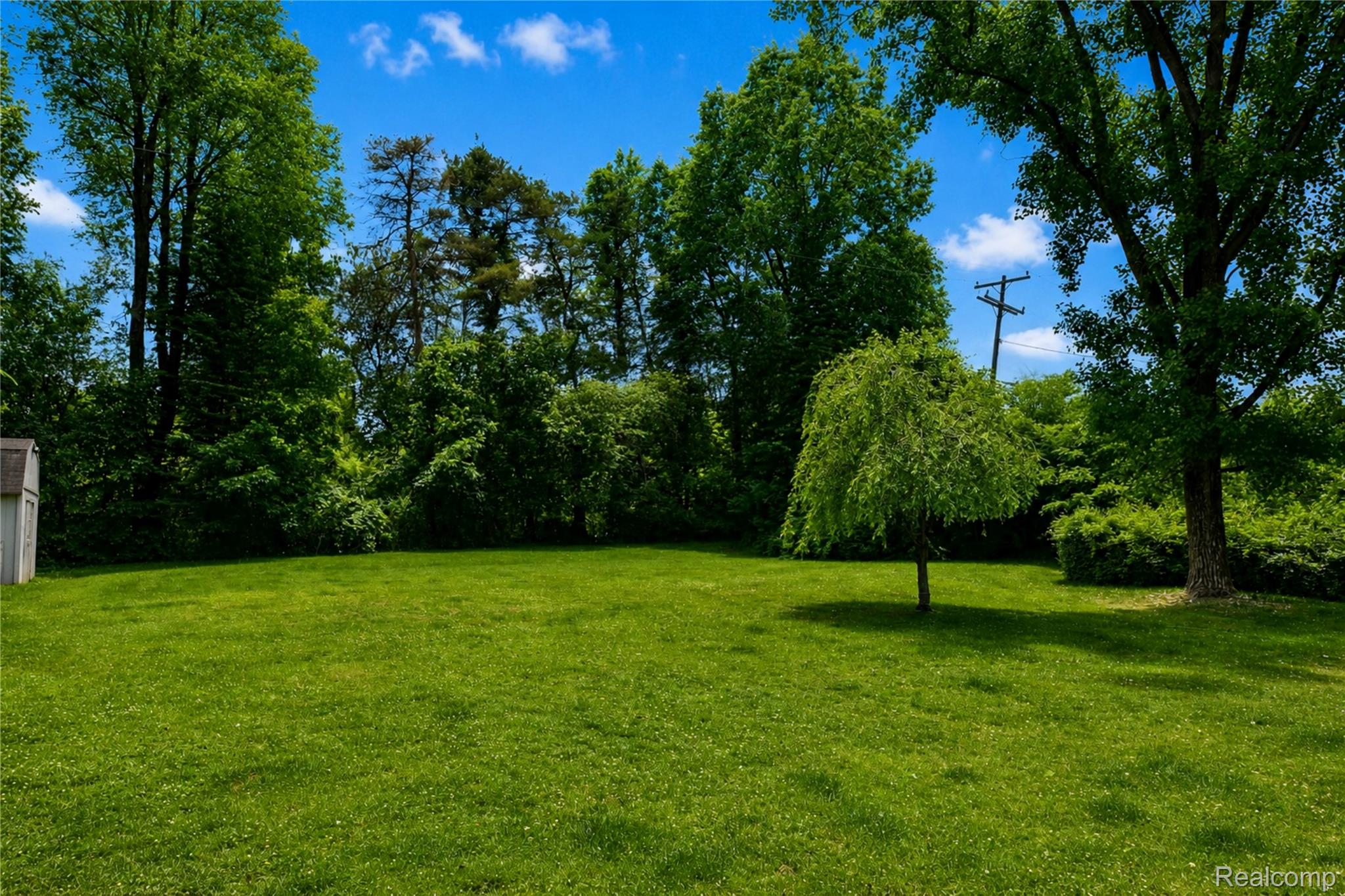1405 Middle Road Highland, MI 48357 - Photo 4 of 18 Expansive green lawn framed by mature trees and varied foliage, featuring a detached storage shed