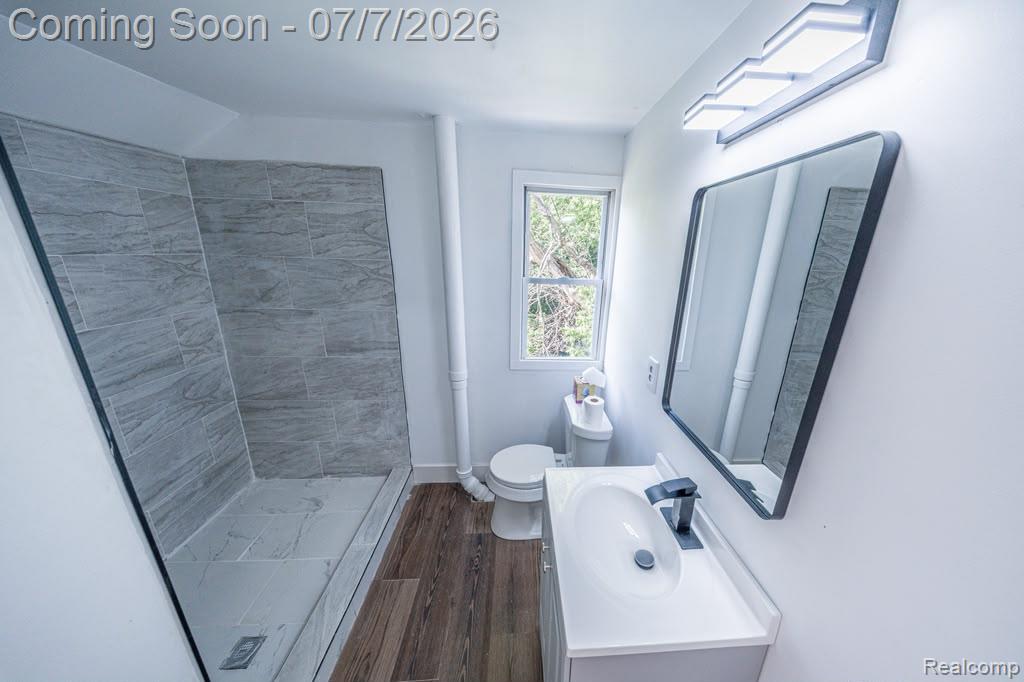 18486 Trinity Street Detroit, MI 48219 - Photo 5 of 19 Bathroom featuring a walk-in shower with gray tile surround, white vanity with integrated sink, black single-handle faucet, rectangular framed mirror, and wood-finish flooring