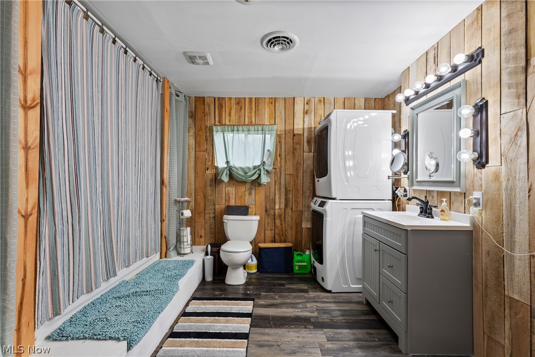 38340 Lees Run Road Cadiz, OH 43907 - Photo 12 of 31 Bathroom featuring wood walls, a shower with curtain, vanity, dark wood-style flooring, and stacked washing machine and dryer