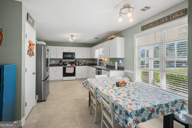 a kitchen with stainless steel appliances granite countertop a refrigerator a stove top oven a sink dishwasher and white cabinets with wooden floor