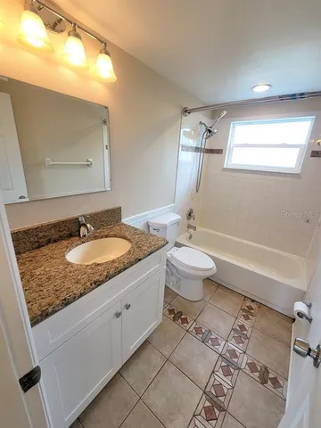 a bathroom with a granite countertop sink a toilet a mirror and bathtub