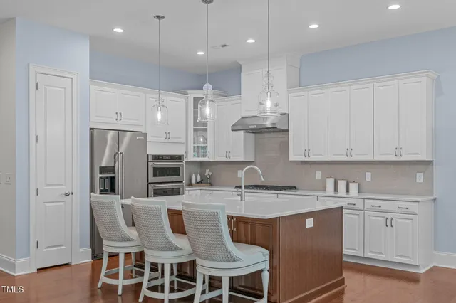 a kitchen with stainless steel appliances granite countertop a sink a stove a refrigerator and white cabinets with wooden floor