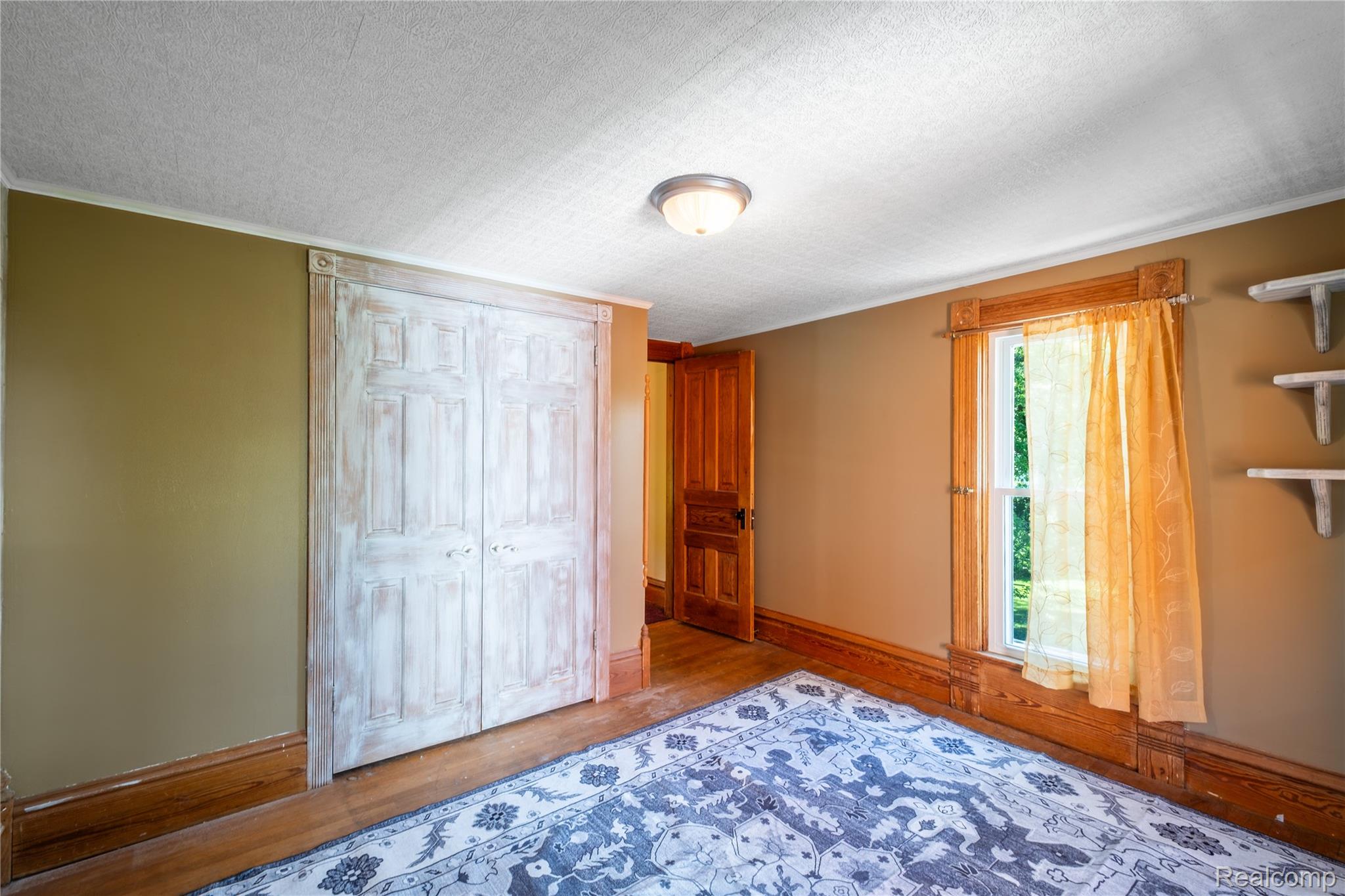 1459 West Cohoctah Road Howell, MI 48855 - Photo 22 of 31 Room featuring wood-finish flooring, a double-panel closet with a distressed finish, and a window with wood trim