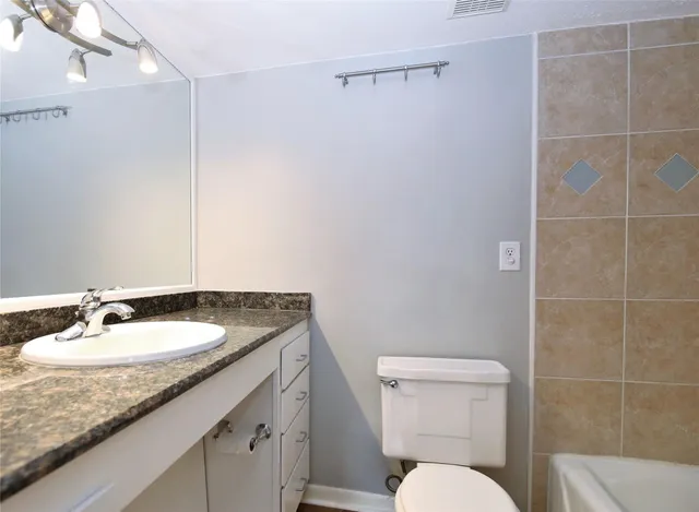 a bathroom with a granite countertop sink a toilet a mirror and shower