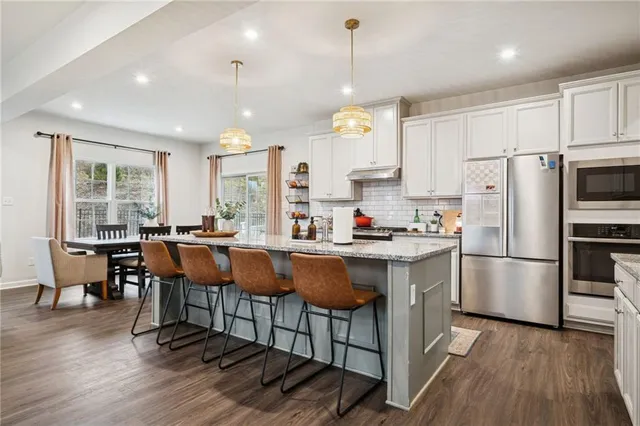 a kitchen with stainless steel appliances granite countertop a refrigerator a sink dishwasher a dining table and chairs with wooden floor