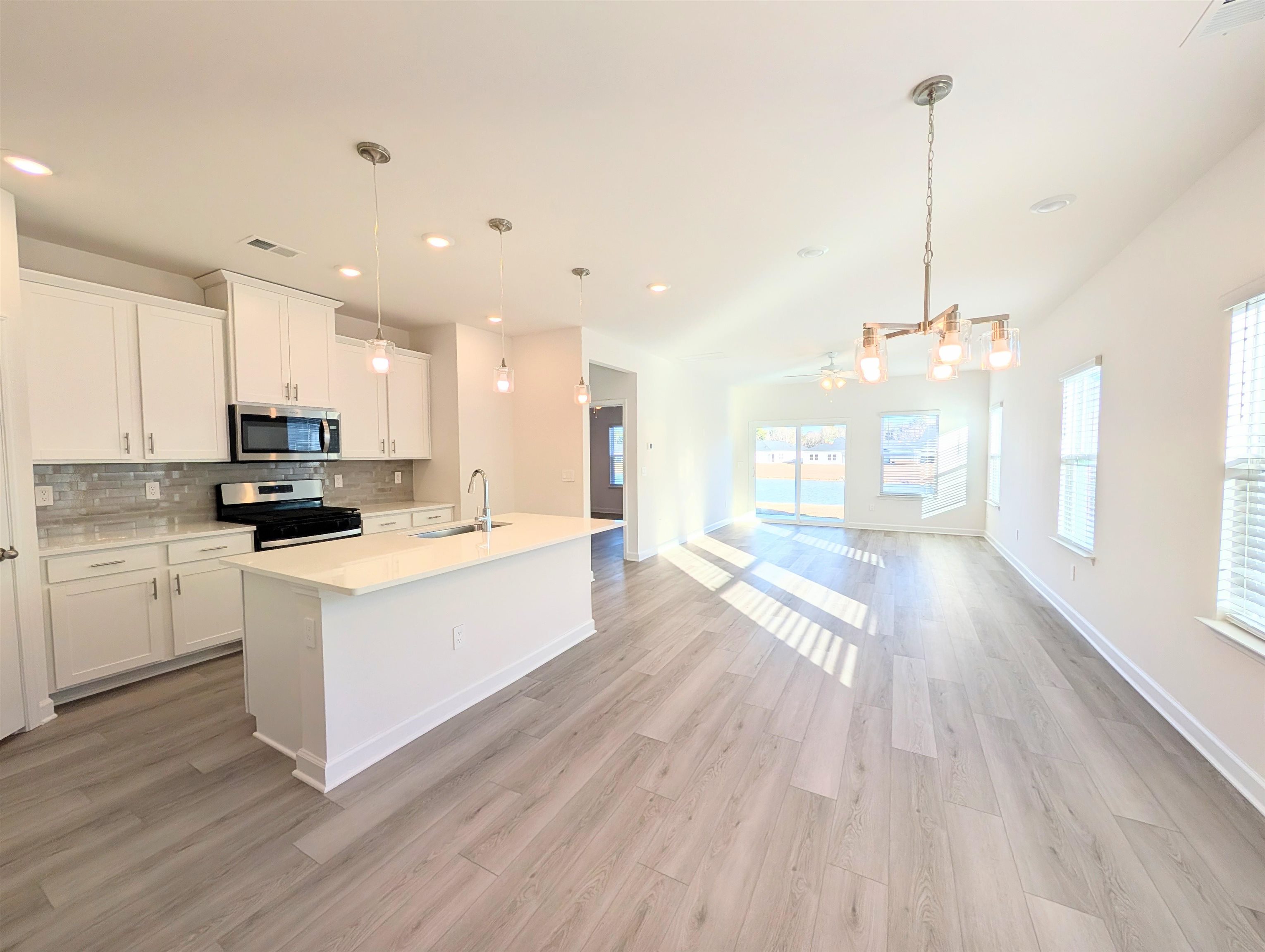 1508 Regal Fern Way Longs, SC 29568 - Photo 6 of 38 Kitchen with decorative light fixtures, stainless steel appliances, a center island with sink, tasteful backsplash, and white cabinets