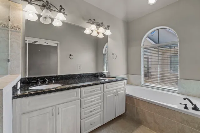 a bathroom with a granite countertop double vanity sink a mirror a lamp and bathtub