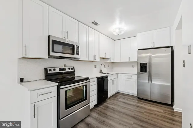 a kitchen with cabinets stainless steel appliances a sink and wooden floor