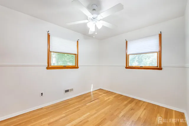 a view of an empty room with wooden floor and a chandelier fan