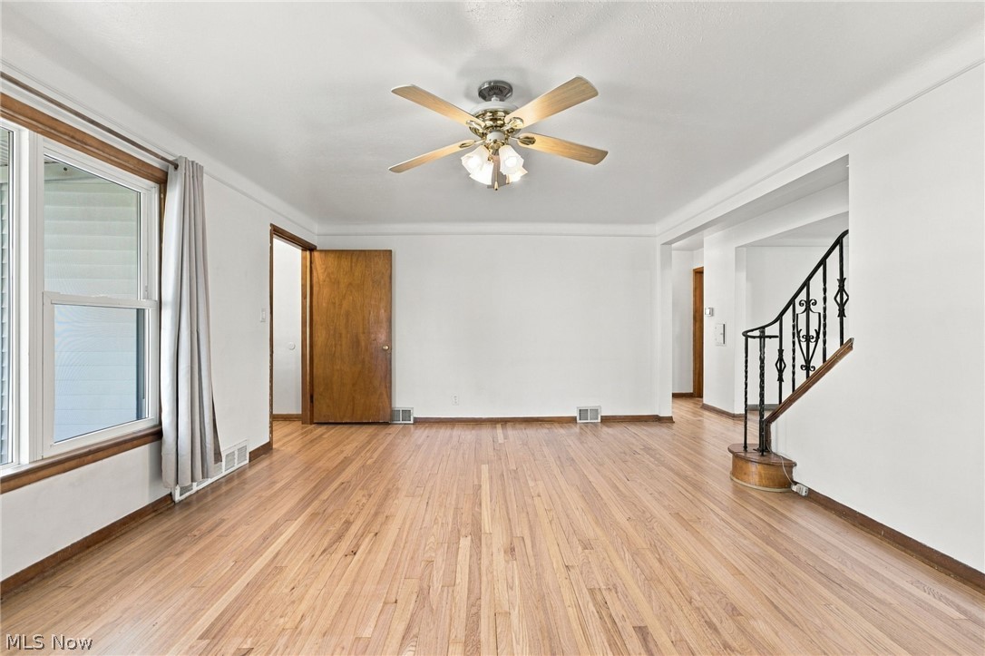 1434 Sunset Road Mayfield Heights, OH 44124 - Photo 2 of 36 Hardwood flooring throughout, white walls, ceiling fan with light, wood-trimmed window, and an ornate metal staircase railing