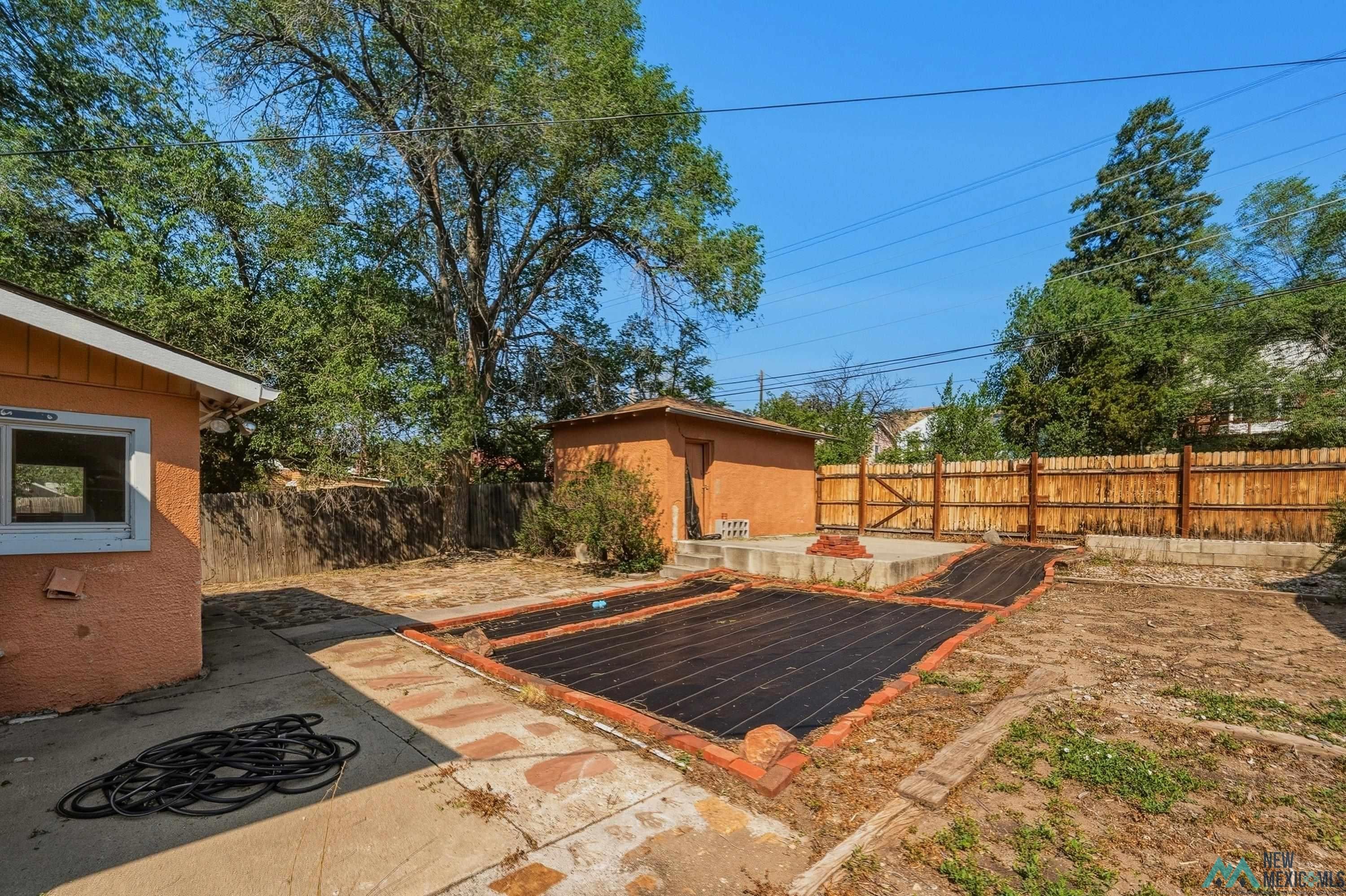 1026 South 5th Street Raton, NM 87740 - Photo 24 of 33 Spacious backyard featuring a wood privacy fence, concrete patio, and a separate stucco outbuilding
