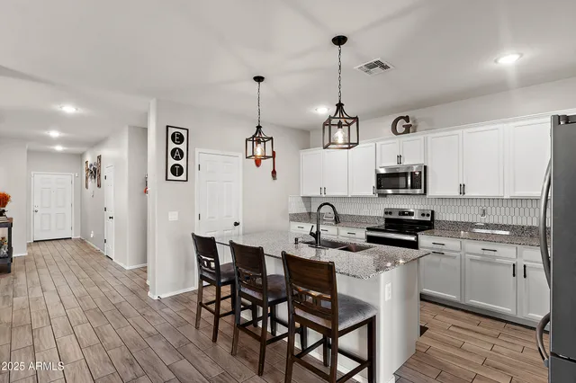 a kitchen with stainless steel appliances kitchen island granite countertop a sink a stove a refrigerator and white cabinets with wooden floor