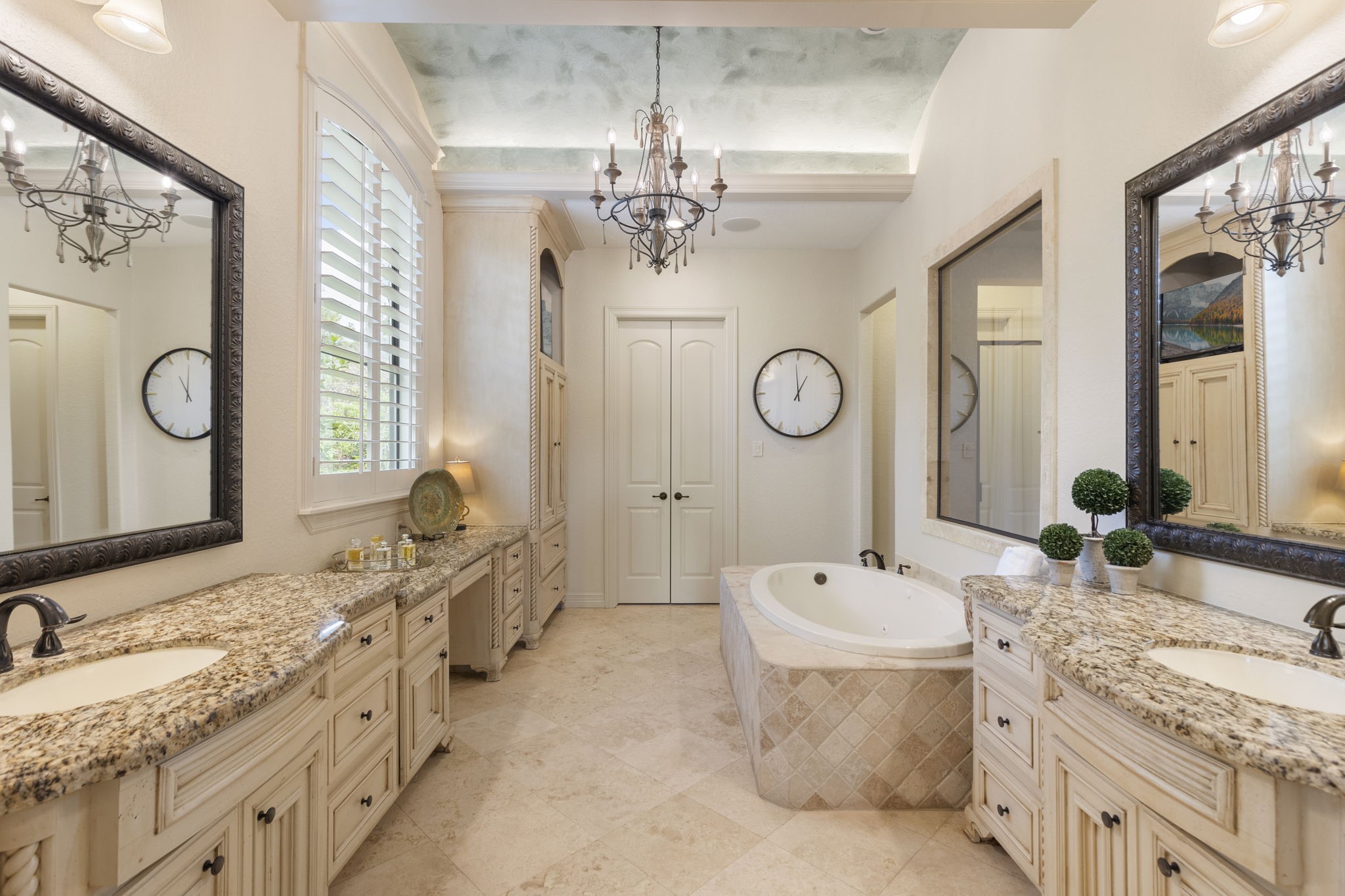 28227 KAILEES Court Spring, TX 77386 - Photo 23 of 48 Grand Primary Bath entered through French doors, featuring Travertine flooring, barrel ceiling with crown molding and accent lighting, decorative chandelier, and integrated sound system. Includes a jetted soaking tub, oversized walk-in shower with bench and tumbled stone accents, dual vanities with granite counters, seated vanity area, built-in linen storage, and an expansive walk-in closet with custom shelving.