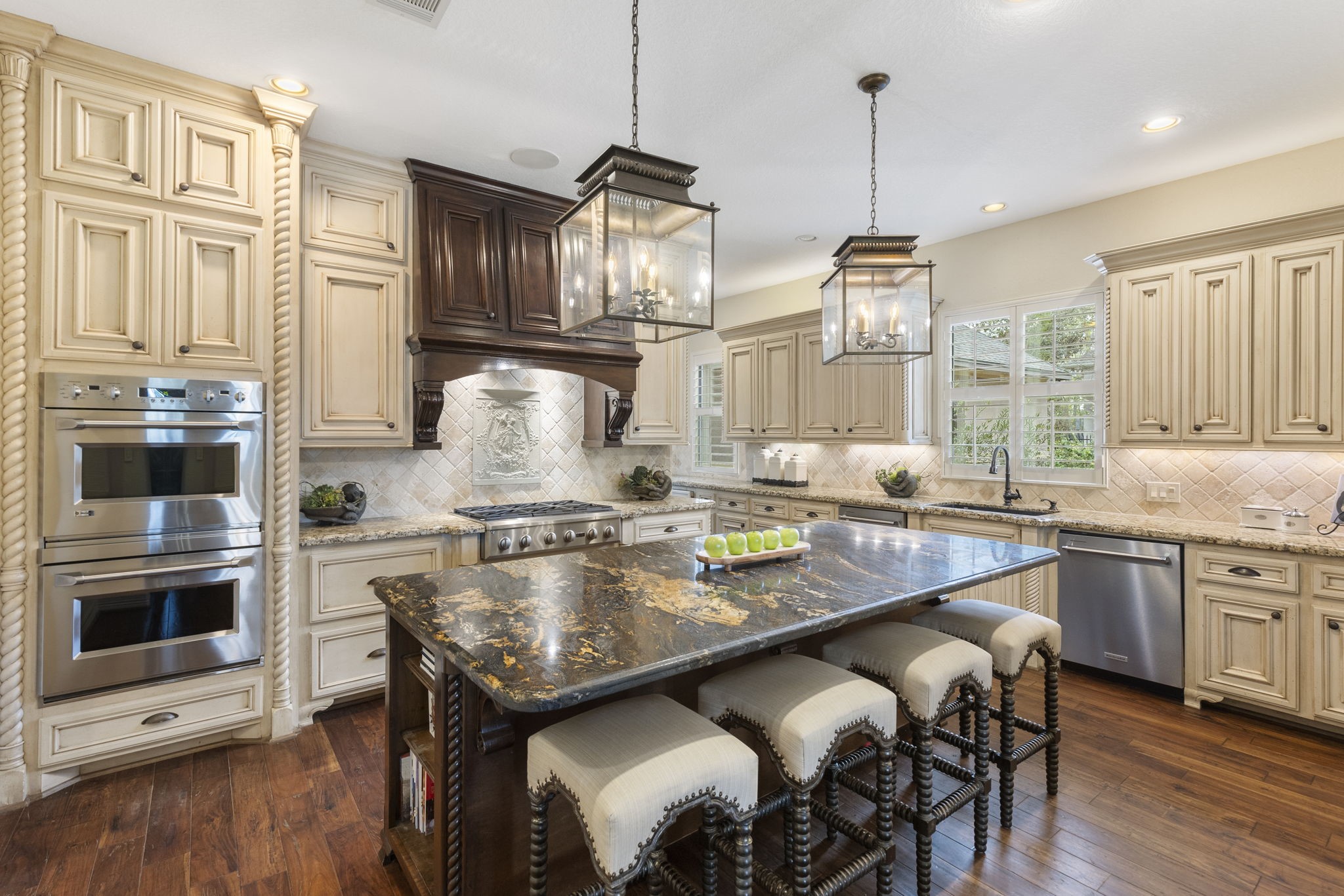 28227 KAILEES Court Spring, TX 77386 - Photo 4 of 48 Stunning Chef’s Kitchen showcasing exceptional craftsmanship with rich wood flooring and a striking accent island featuring high-end granite, seating, built-in microwave, and lantern-style pendant lighting.