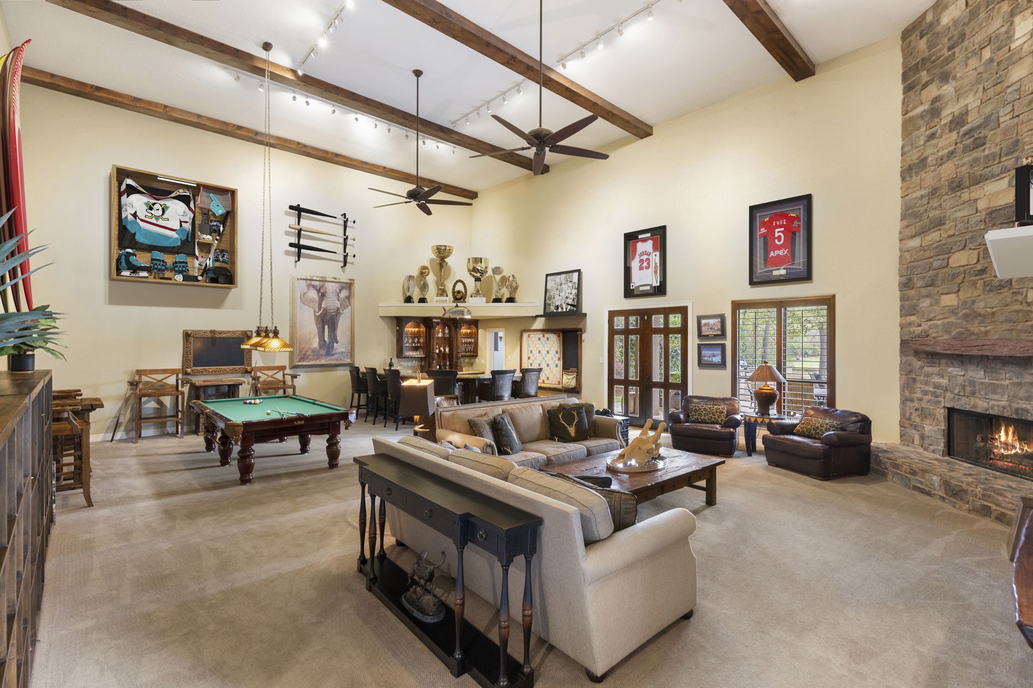 28227 KAILEES Court Spring, TX 77386 - Photo 5 of 48 Truly one-of-a-kind Game/Trophy Room spanning nearly 1,200 SF of incredible entertaining space, featuring soaring two-story ceilings with wood beams, floor-to-ceiling stone fireplace, full bar setup, integrated sound system, and dual French doors opening to the back patio. *Partially Virtually Staged Image