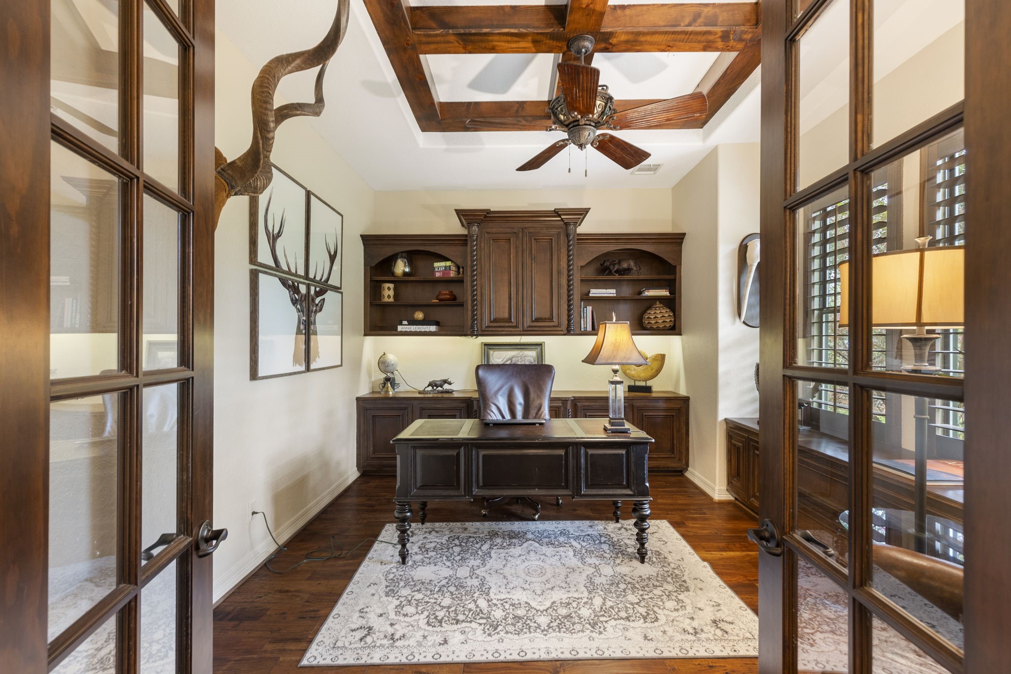 28227 KAILEES Court Spring, TX 77386 - Photo 9 of 48 Distinguished Executive Study with glass French doors, wood flooring, and a striking beam-coffered ceiling. Custom built-ins and credenza provide refined functionality, complemented by plantation shutters and a ceiling fan for comfort.