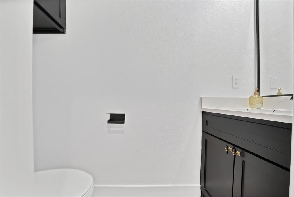 805 Tierney Road Fort Worth, TX 76112 - Photo 16 of 36 Black vanity with gold-finish hardware, a white countertop, and a framed mirror