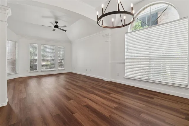 an empty room with wooden floor chandelier fan and windows