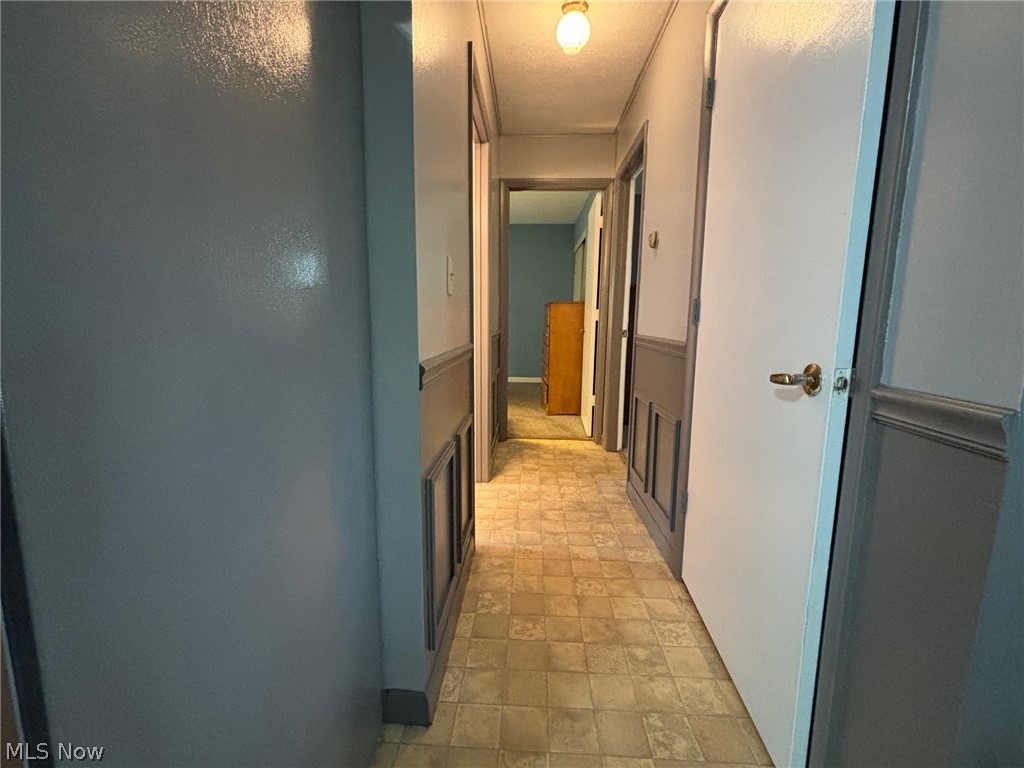 57575 Marietta Road Byesville, OH 43723 - Photo 7 of 25 Hallway featuring patterned vinyl flooring, a flush-mount ceiling light fixture, panel wainscoting, and white interior doors with brass hardware