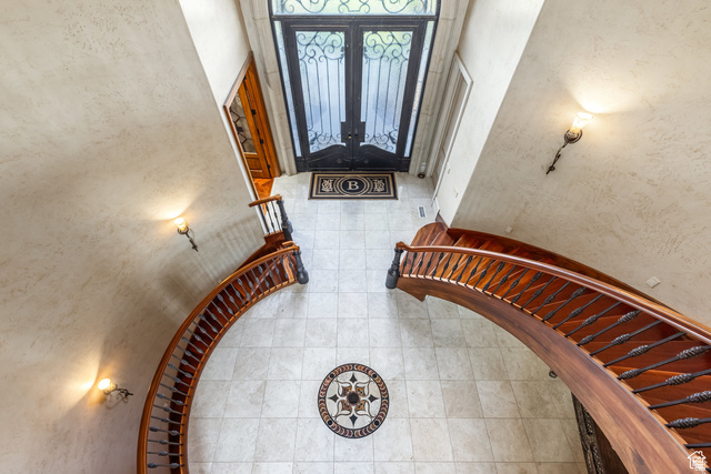 694 West Cephus Road Draper, UT 84020 - Photo 11 of 148 Grand entryway featuring twin curved staircases with ornate wrought iron balusters and wood handrails, a decorative tile floor inlay, and a dark wood entry door with wrought iron detailing