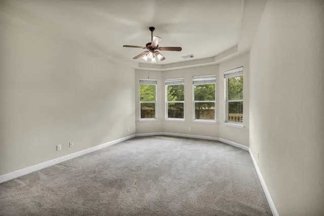 an empty room with chandelier fan and windows