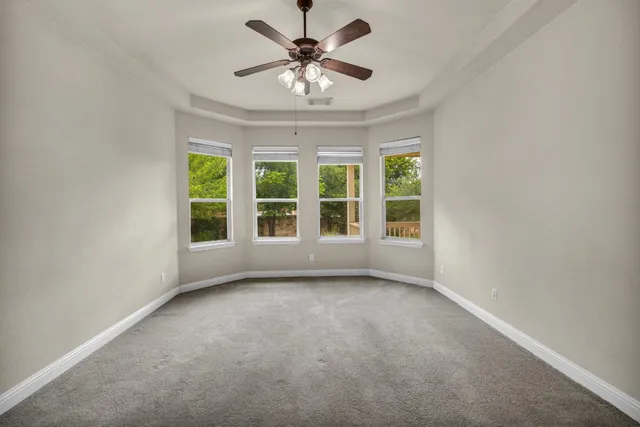 an empty room with chandelier fan and windows