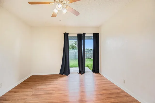 a view of an empty room with wooden floor and a ceiling fan