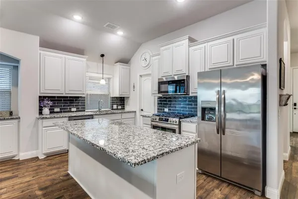 a kitchen with kitchen island granite countertop a refrigerator a stove a sink and white cabinets with wooden floor