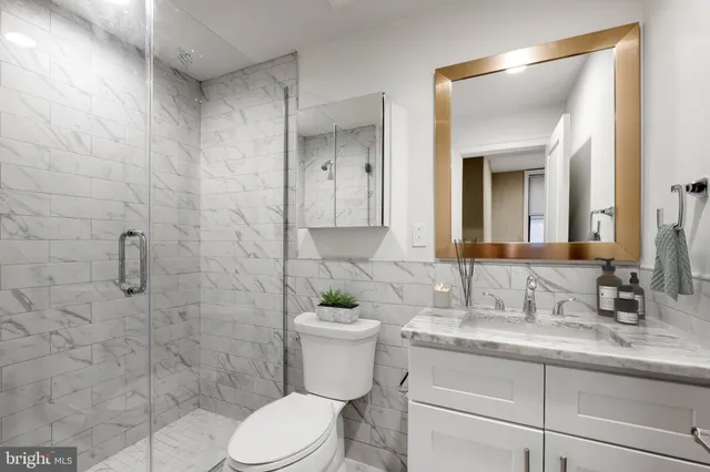 a bathroom with a granite countertop sink a toilet a mirror and shower