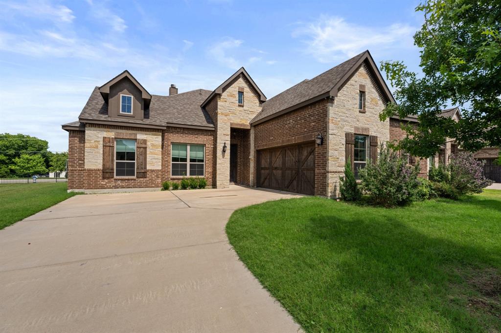 View of front of house featuring driveway, a front lawn, a shingled roof, stone siding, and brick siding