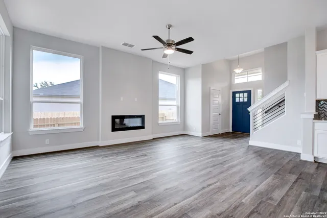 an empty room with wooden floor a ceiling fan and windows