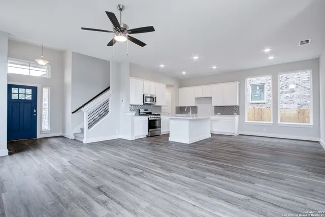 a view of an empty room with wooden floor and a kitchen