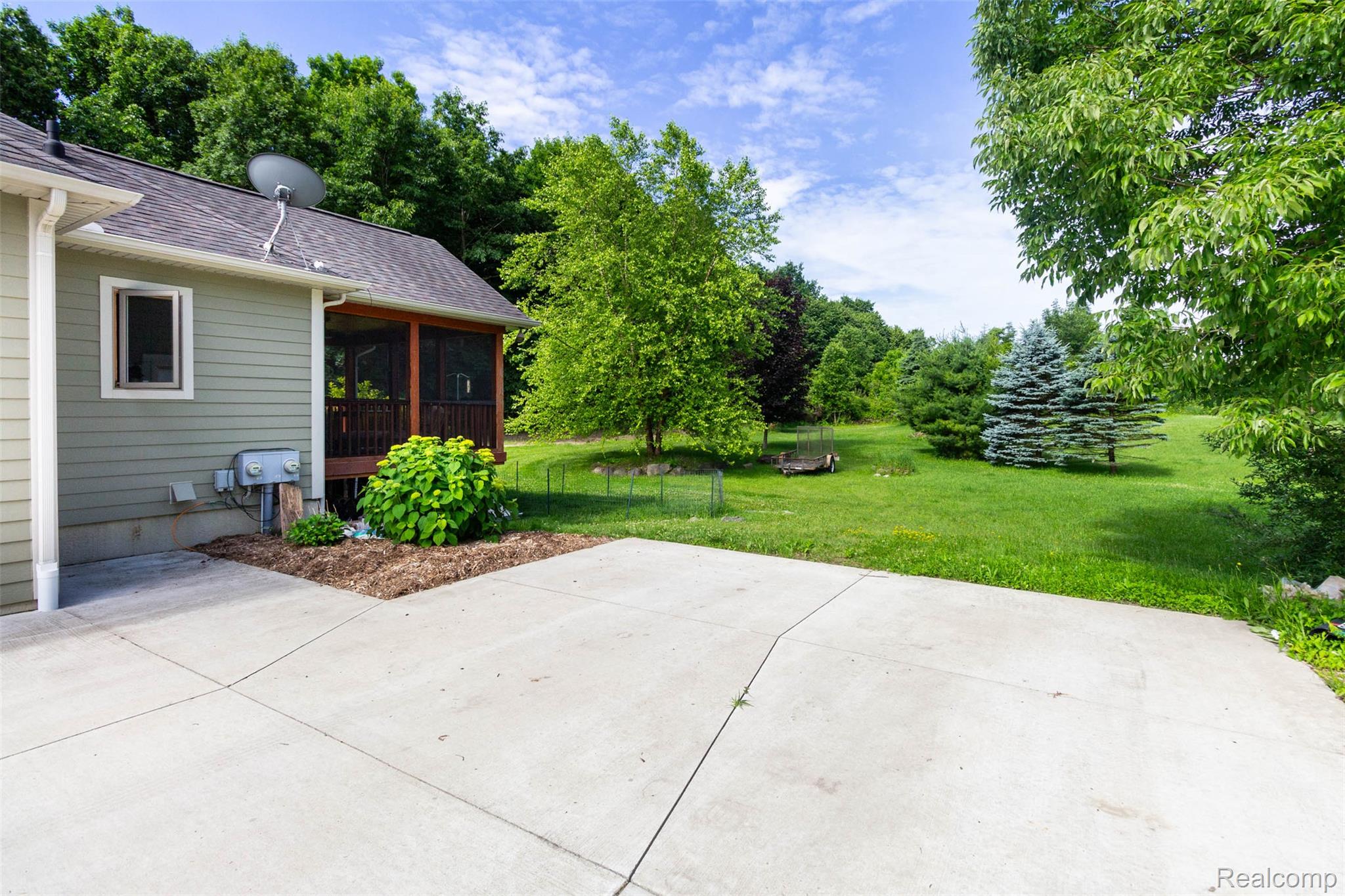9887 Hadley Road Clarkston, MI 48348 - Photo 36 of 56 Expansive concrete patio with a screened-in porch, surrounded by lush green lawn and mature trees