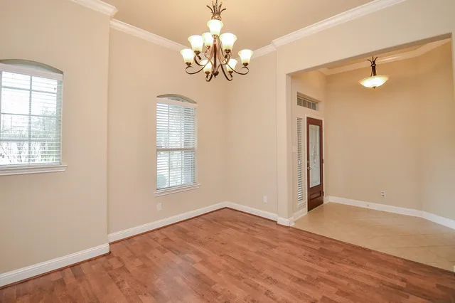 an empty room with wooden floor chandelier and windows