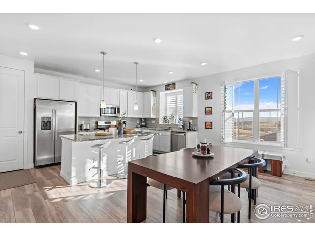 a kitchen with stainless steel appliances kitchen island granite countertop a refrigerator a stove a sink a dining table and chairs with wooden floor