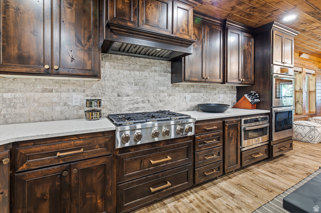 2031 South Quakie Road Koosharem, UT 84744 - Photo 12 of 33 Dark wood cabinetry, stainless steel oven, cooktop, and microwave, light-toned stone backsplash, and light-toned countertops