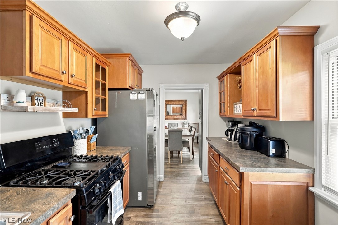 1875 Perth Road Madison, OH 44057 - Photo 7 of 48 Galley kitchen featuring wood-finish cabinetry, dark countertops, wood-finish flooring, a ceiling-mounted light fixture, and a window with blinds