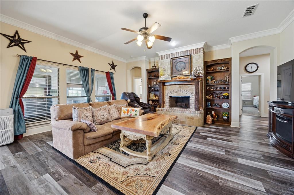 119 George Owens Road Ponder, TX 76259 - Photo 5 of 26 Spacious living area featuring wood-finish flooring, an arched brick fireplace with built-in shelving, decorative crown molding, and multiple windows with blinds