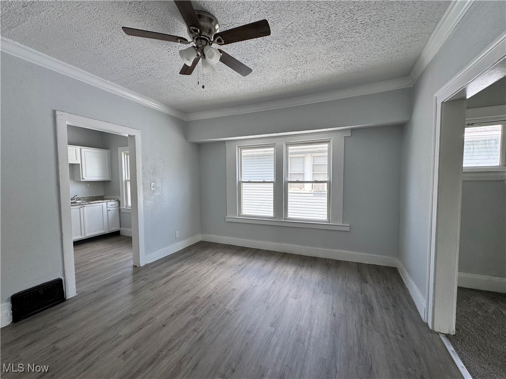 3624 East 118th Street Cleveland, OH 44105 - Photo 28 of 49 Unfurnished living room with a textured ceiling, a ceiling fan, crown molding, and dark wood-type flooring